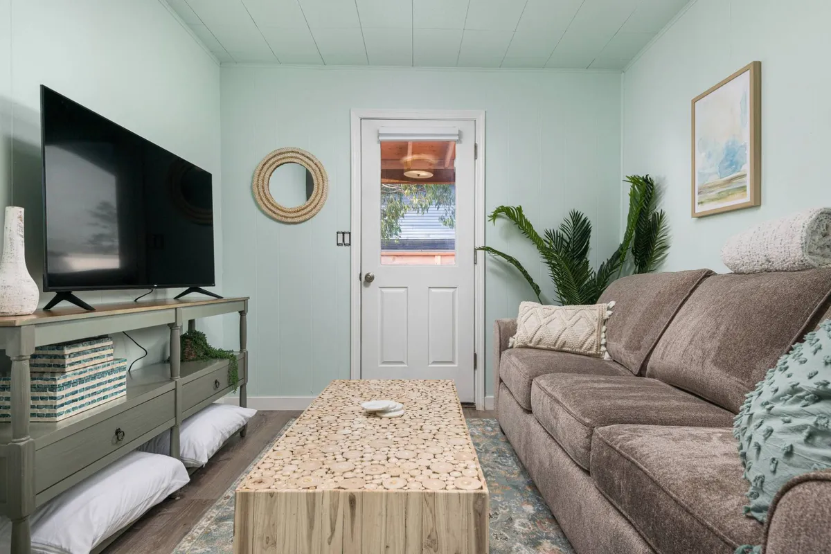 This image features a cozy living area with a sofa, coffee table, television, and a visible door, creating a welcoming space for relaxation and casual socializing. The positioning of the door subtly hints at the connection between private interiors and the wider community outside.