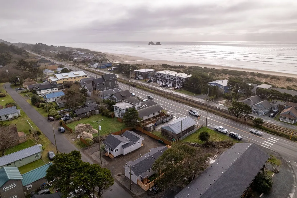 This image captures a wide swath of sandy beach meeting the gentle Pacific waves, with seaside houses and a road nearby. The serene ambiance and soft evening light evoke the feeling of strolling just steps from a cottage to the shore. The proximity of homes to the beach is visually clear, aligning with the section’s emphasis on easy, immediate access.