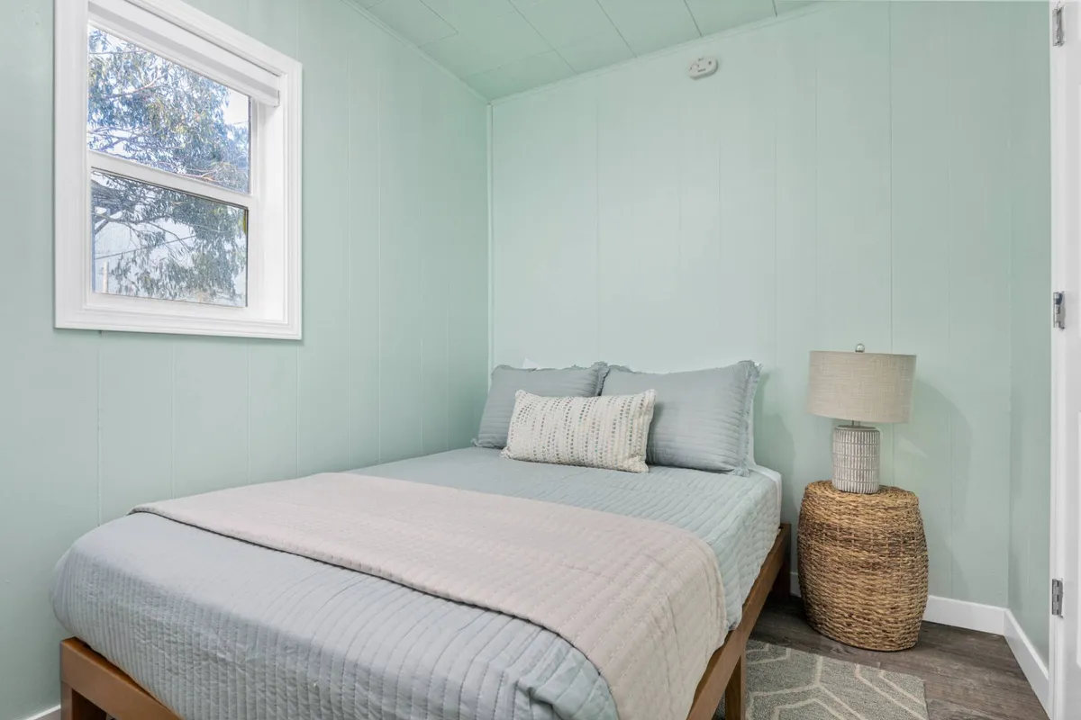 A serene bedroom with a neatly made bed, a soft lamp casting warm light, and a window inviting gentle natural light into the space. The uncluttered setting creates an atmosphere of tranquility and relaxation, perfect for restful sleep or quiet reading.