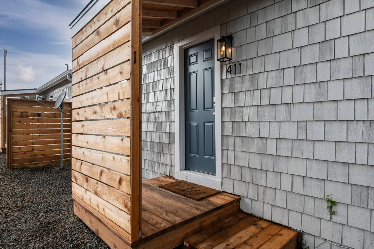 A close-up of the front door with wooden steps and textured siding, creating an inviting entrance. The scene suggests a welcoming return after a day out, with personal touches and approachable charm.