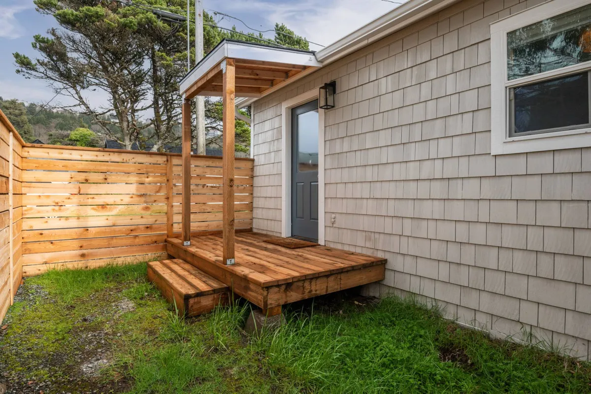 A welcoming exterior featuring wooden steps leading to a private front door, bordered by a fenced yard perfect for pets. The space invites guests to enjoy morning coffee or host small gatherings, blending private relaxation with pet-friendly convenience.