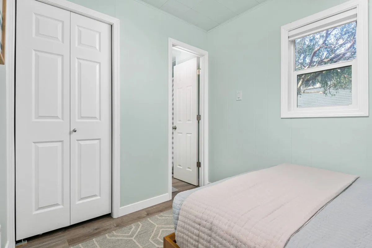 A calm, inviting bedroom scene featuring closet doors, a window, and a comfortable bed dressed in quality linens. The natural light suggests a gentle start to the day and the overall setup feels cozy and private.