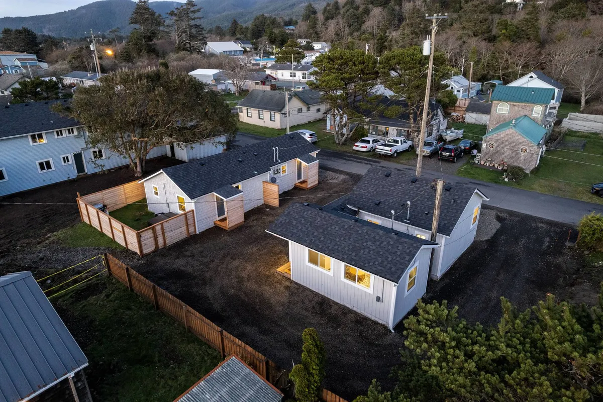 A wide view showcasing multiple small cottages nestled among trees with a mountain backdrop. The communal layout and surrounding greenery evoke the sense of a connected, vibrant, and picturesque neighborhood—ideal for guests eager to explore on foot.