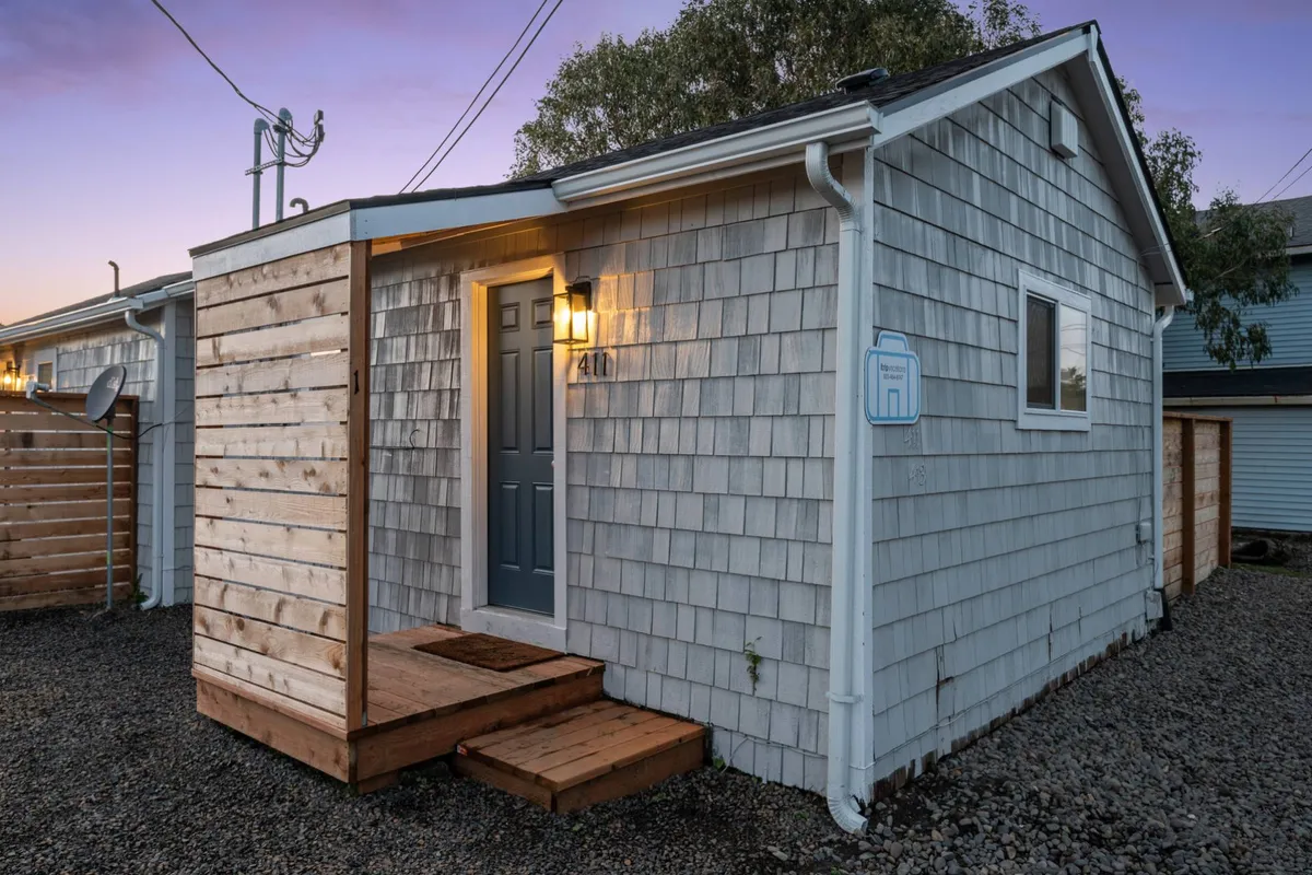 A welcoming exterior shot of the front door, with wooden steps and a softly lit porch area. The inviting setting suggests easy access to walks and outdoor activities, as well as spaces to meet neighbors and enjoy the fresh air with a pet. The evening light adds a cozy, communal touch.