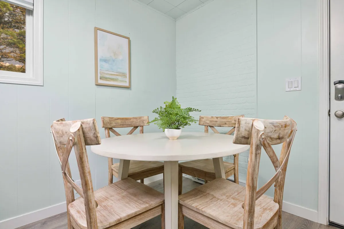 A round wooden dining table with comfortable chairs, a potted plant, and wall art, creating a warm and intimate spot for meals, games, or conversations. The decor is updated and welcoming, aligning with the cottage’s modern and inviting atmosphere.